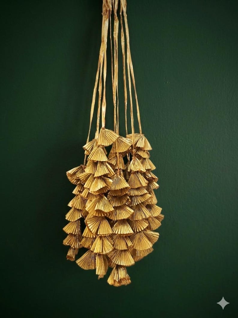 May include: A collection of gold-coloured, fan-shaped tassels suspended against a dark green backdrop. The tassels are constructed from layered, textured material and hang from long, thin strands. The overall appearance is decorative and elegant.