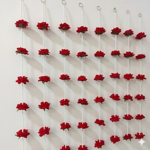 Puede incluir: Guirnaldas de rosas rojas con cuentas blancas perladas colgando de anillos metálicos. Las guirnaldas están dispuestas en filas verticales sobre un fondo blanco, creando una exhibición floral decorativa. Cada guirnalda presenta múltiples rosas rojas.