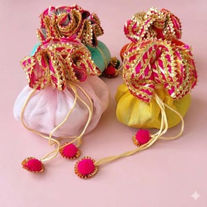 Peut inclure: Quatre pochettes colorées à cordon. Les pochettes sont dans les tons de rose, jaune et sarcelle, avec des garnitures décoratives dorées et roses. Chaque pochette a un cordon assorti avec un pompon rose.