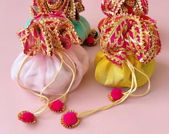 May include: Four colorful drawstring pouches. The pouches are in shades of pink, yellow, and teal, with gold and pink decorative trim. Each pouch has a matching drawstring with a pink pom-pom accent.
