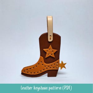 Op de afbeelding: Een bruinleren cowboylaars-sleutelhanger met een tan ster en spoor detail. De sleutelhanger heeft een tan lus aan de bovenkant. De tekst "leather keychain pattern (PDF)" staat onderaan.