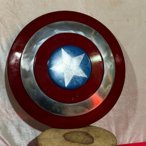 May include: A circular shield featuring a red border, a silver central band, and a blue central disc with a white star. This shield is a replica of Captain America's shield.