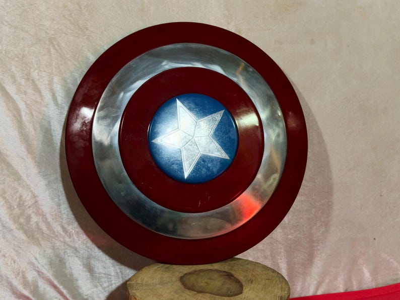 May include: A circular shield featuring a red border, a silver central band, and a blue central disc with a white star. This shield is a replica of Captain America's shield.