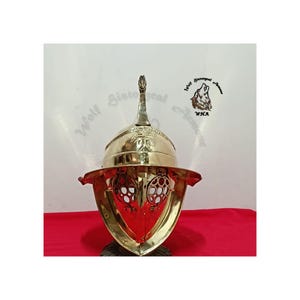 Può includere: Un elmo da gladiatore in ottone lucido con una cresta centrale, una tesa larga e due protezioni oculari circolari con un motivo a reticolo decorativo. L'elmo presenta un motivo a palma inciso sulla parte anteriore e il logo Wolf Historical Armour.