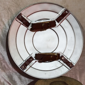 May include: A silver shield featuring concentric circles and brown leather straps with gold buckles. The shield is circular and has a metallic finish. The diameter is approximately 60 cm.
