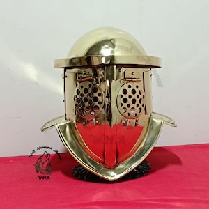 Può includere: Un elmo da gladiatore in ottone lucido con cupola arrotondata, tesa larga e due piastre facciali circolari incernierate con fori di ventilazione perforati. La parte anteriore dell'elmo presenta una cresta centrale verticale e un paranuca.