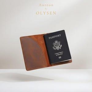 May include: A brown leather passport holder with a black passport inside. The passport is open, displaying the words "PASSPORT" and "United States of America". The brand name "Aureon by OLYSEN" is at the top.