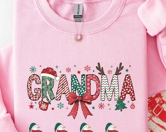 May include: Pink sweatshirt with the word "Grandma" in a festive design. The letters are decorated with Christmas elements like a Santa hat, reindeer antlers, and a bow. Below are snowmen with names.