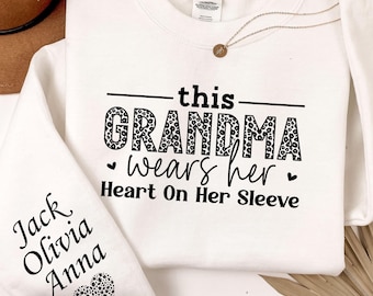 May include: White sweatshirt with the text "this GRANDMA wears her Heart On Her Sleeve" in black and leopard print. The left sleeve has the names "Jack Olivia Anna" and a leopard print heart.