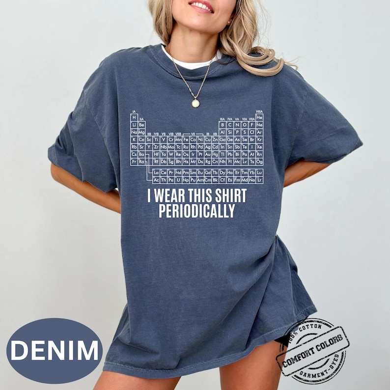 Może przedstawiać: Niebieska koszulka dżinsowa z białym wzorem układu okresowego i napisem "I wear this shirt periodically." Koszulka jest wykonana w 100% z bawełny i farbowana w kawałku.