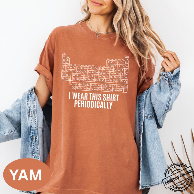 Może przedstawiać: Rdzawa koszulka z białym wzorem układu okresowego i napisem "I WEAR THIS SHIRT PERIODICALLY". Koszulka wykonana jest w 100% z bawełny i ma wykończenie barwione w technologii Comfort Colors.