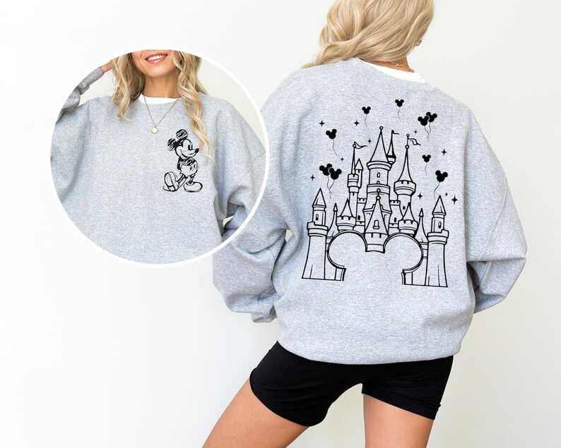 Puede incluir: Una sudadera gris claro con un dise&ntilde;o de Mickey Mouse en blanco y negro en la parte delantera. La parte trasera de la sudadera muestra un dise&ntilde;o de castillo en blanco y negro, orejas de Mickey Mouse y globos.