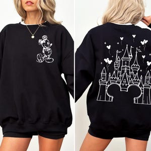 Puede incluir: Sudadera negra con un dise&ntilde;o de Mickey Mouse blanco en la parte delantera y un castillo en la parte trasera. La sudadera tiene cuello blanco y mangas largas. El dise&ntilde;o presenta una silueta de castillo con orejas de Mickey.