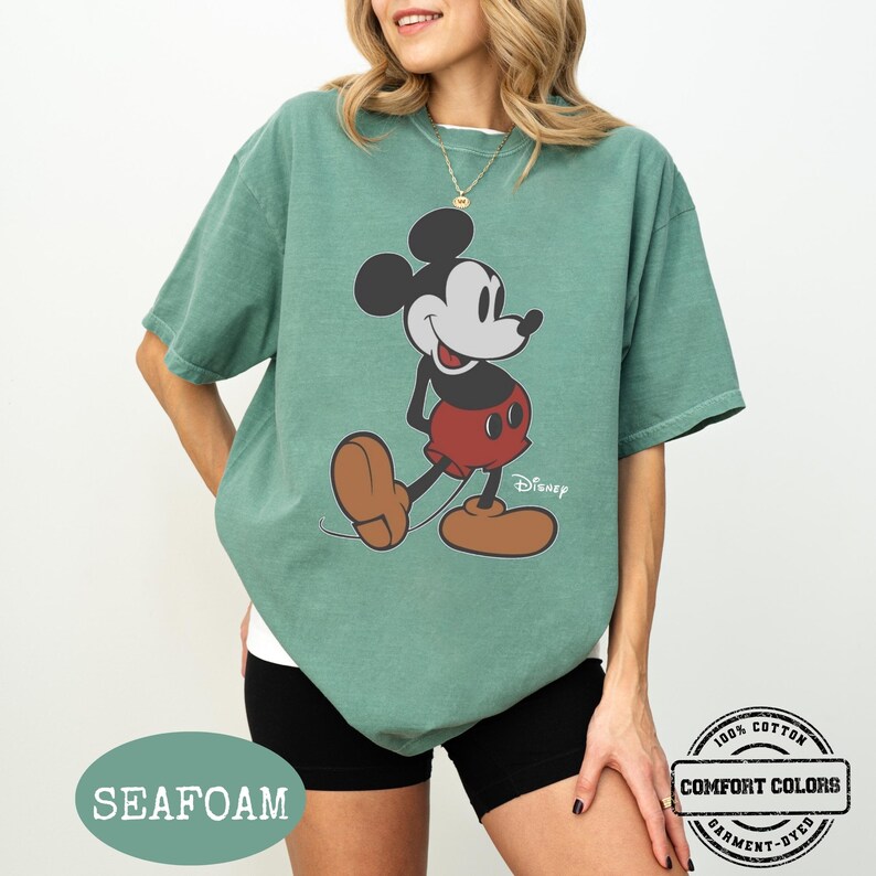 May include: Seafoam green t-shirt with a Mickey Mouse graphic. The cartoon character is in black, red, and brown. The shirt is labelled "Comfort Colors" and is made of 100% cotton.