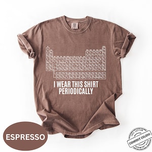 Może przedstawiać: Koszulka w kolorze espresso z białym wzorem układu okresowego i napisem "I Wear This Shirt Periodically". Koszulka jest wykonana w 100% z bawełny i farbowana w kawałku.