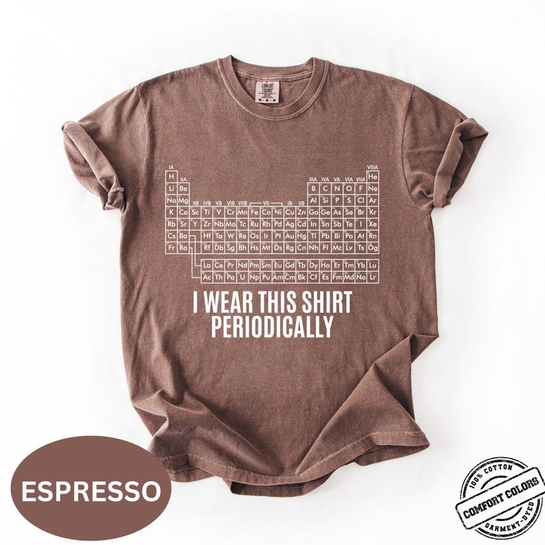 Może przedstawiać: Koszulka w kolorze espresso z białym wzorem układu okresowego i napisem "I Wear This Shirt Periodically". Koszulka jest wykonana w 100% z bawełny i farbowana w kawałku.