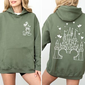 Puede incluir: Sudadera con capucha verde oliva con bolsillo delantero y capucha. La parte delantera presenta un boceto blanco de Mickey Mouse. La parte posterior muestra un dise&ntilde;o de castillo blanco con orejas de Mickey Mouse, globos y estrellas. Una sudadera casual y c&oacute;moda.