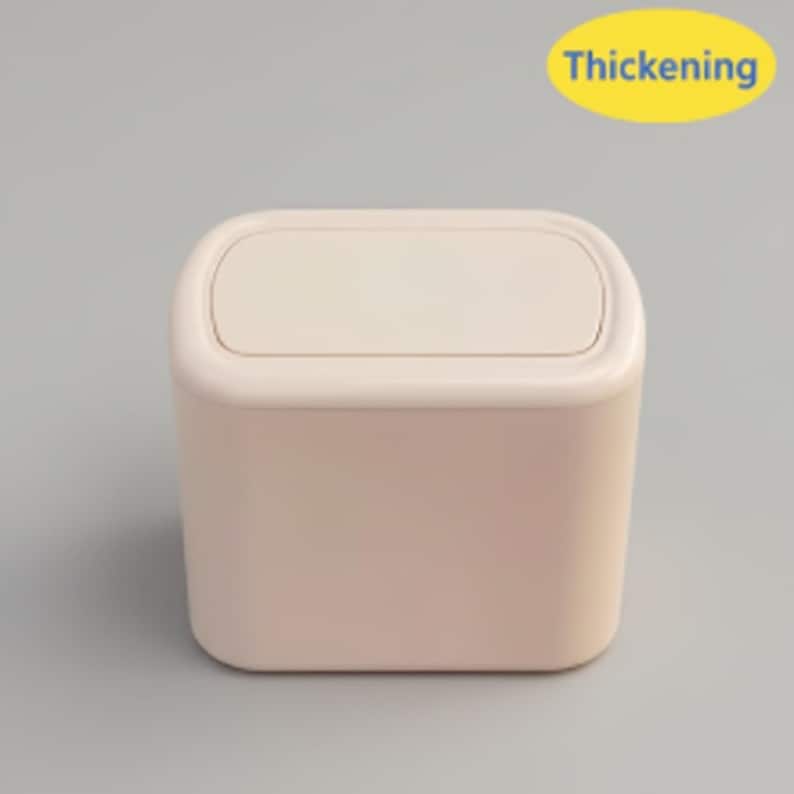 May include: A small, rectangular, light pink trash can with a matching lid. The lid has a slightly rounded shape and fits snugly on top. The words "Thickening" are in a yellow oval in the upper right corner.