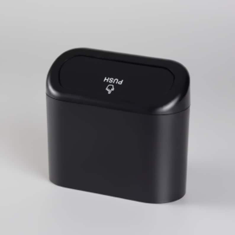 May include: A black, rectangular trash can with a rounded top. The lid has the word "PUSH" and a small graphic. The can is designed with a smooth, matte finish.