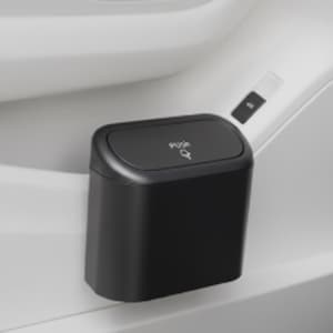 May include: A small, black, rectangular trash can with a rounded top. The lid is labeled "Push" with a small arrow. The trash can is mounted on a white surface, likely in a vehicle.