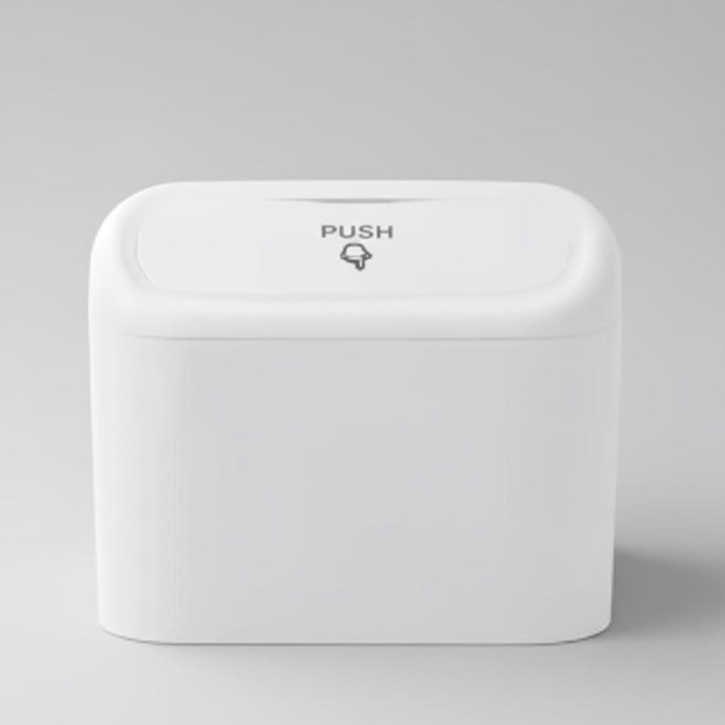 May include: A white, rectangular waste bin with rounded corners. The top of the bin has the word "PUSH" printed in gray, along with a bell icon. The bin is made of a smooth, solid material.