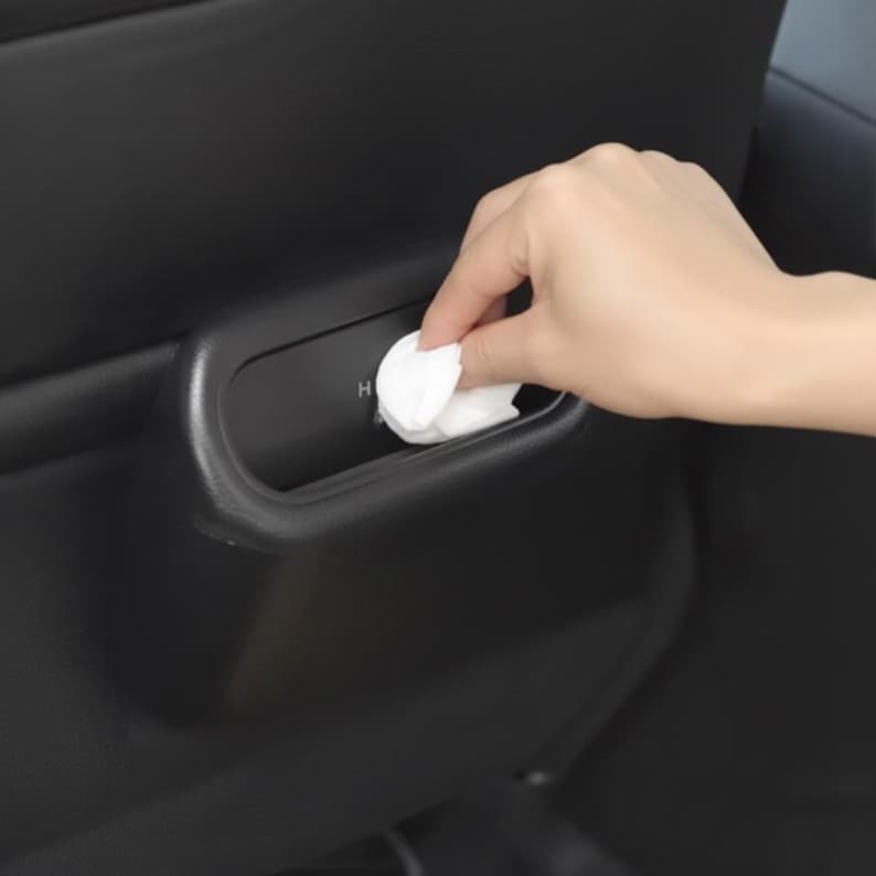 May include: A hand placing a white wipe into a black car interior compartment. The compartment has a curved design and the letter "H" is visible. The car interior is black.