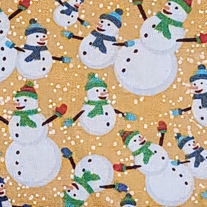 以下が含まれることがあります： 質感のあるゴールドの背景に、複数の白い雪だるまが描かれた生地のパターン。雪だるまは緑や青などの様々な色のスカーフと帽子を身につけ、赤いミトンをしています。デザイン全体に小さな白い点が散りばめられています。