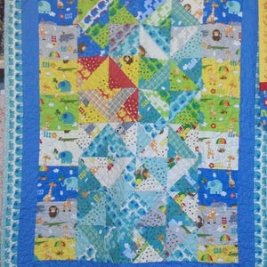 Peut inclure: Une courtepointe rectangulaire en patchwork présentant un motif répétitif d'animaux de dessin animé, notamment des girafes, des éléphants et des singes. Elle est composée de divers carrés de tissu dans des tons de bleu, vert, jaune et rouge.