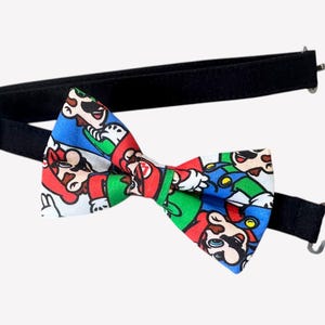 Puede incluir: Una pajarita negra con una correa ajustable y un estampado colorido con los personajes de Mario y Luigi.