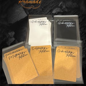Könnte beinhalten: Geschenkanhänger in transparenten Kunststoffhüllen. Die Anhänger sind weiß, schwarz und braun, mit handschriftlichem Schriftzug in schwarzer Tinte. Das Wort "Prämade" steht in Gold oben. Geeignet für verschiedene Anlässe.