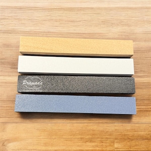 Puede incluir: Cuatro muestras rectangulares de madera. La superior es de color beige claro, la segunda blanca, la tercera gris oscuro con la palabra "Prämade" impresa y la inferior azul claro.