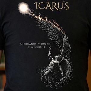 May include: Black t-shirt featuring a detailed graphic of Icarus, with the word "ICARUS" in gold lettering at the top. The design includes a falling figure with wings, a sun, and the words "ARROGANCE + HUBRIS PUNISHMENT".