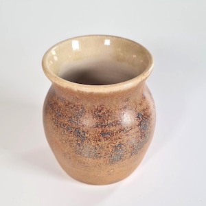 May include: A ceramic vase with a rounded body and a wide, flared rim. The exterior features a mottled texture with earthy brown and muted blue tones, while the interior has a smooth, light beige glaze that extends over the top edge.