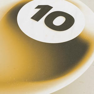 May include: A close-up of a white and gold billiard ball with the number 10 in black on a white circle. The ball has a gradient effect, transitioning from gold to black.