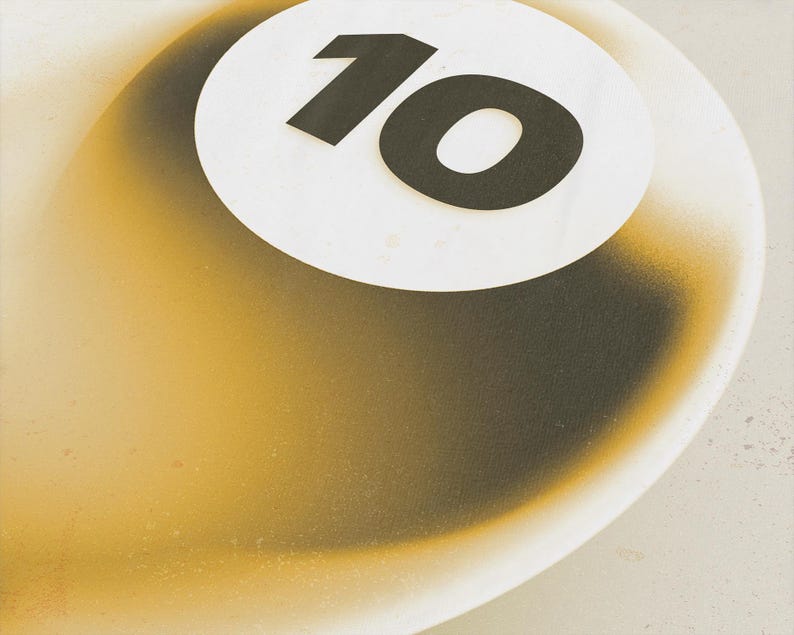 May include: A close-up of a white and gold billiard ball with the number 10 in black on a white circle. The ball has a gradient effect, transitioning from gold to black.