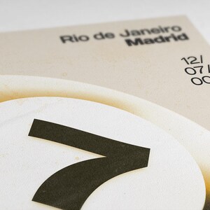 May include: Close-up of a design with the words "Rio de Janeiro Madrid" in black font. A large white circle with a black "7" is in the foreground. The date "12/07/001" is also visible. The background is a light beige color.