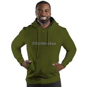 May include: Olive green hooded sweatshirt with the text "Ji Kurdistanê me" in a cursive font across the chest. The sweatshirt has a kangaroo pocket and a drawstring hood. The model is smiling.