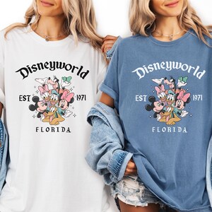 Puede incluir: Camisetas blancas y azules con un gr&aacute;fico de Disneyworld. El gr&aacute;fico incluye el texto "Disneyworld EST 1971 FLORIDA" con los personajes de dibujos animados Mickey Mouse, Minnie Mouse, Donald Duck, Daisy Duck, Goofy y Pluto.