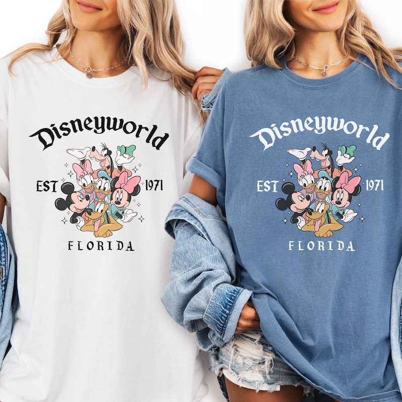 Puede incluir: Camisetas blancas y azules con un gr&aacute;fico de Disneyworld. El gr&aacute;fico incluye el texto "Disneyworld EST 1971 FLORIDA" con los personajes de dibujos animados Mickey Mouse, Minnie Mouse, Donald Duck, Daisy Duck, Goofy y Pluto.