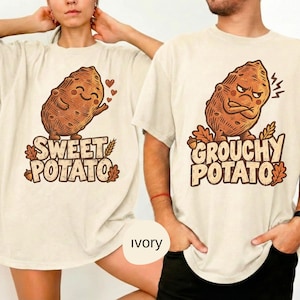 May include: Two ivory t-shirts featuring brown graphic prints. The left shirt displays a smiling potato with the text "SWEET POTATO" and small hearts. The right shirt shows an angry potato with crossed arms and the text "GROUCHY POTATO".