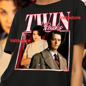May include: Black t-shirt with a Twin Peaks graphic, including the show's title and character images. The shirt is worn by a person with blonde hair and blue earrings. The background has a red border and lightning bolts. The text "Valtastore" is visible.