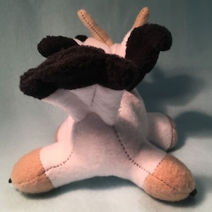 K&ouml;nnte beinhalten: Ein wei&szlig;es und schwarzes Pl&uuml;schtier-Kuh mit braunen Hufen. Die Kuh liegt auf der Seite mit dem Kopf zur Seite gedreht. Die Kuh hat ein schwarz-wei&szlig;es geflecktes Muster.