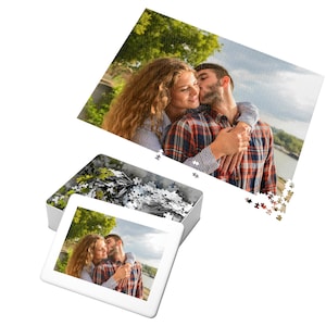 May include: A white metal puzzle box with a printed image of a couple kissing. The box is open, revealing a pile of puzzle pieces. A completed puzzle of the same image is also visible.