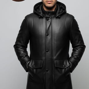 May include: Black leather hooded coat with two front pockets and button closures. The coat has a tailored fit and a sleek, modern design. The coat is from Rustic Hidecraft.