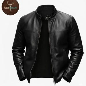 K&ouml;nnte beinhalten: Eine schwarze Lederjacke mit Stehkragen und Druckknopfverschluss, einem durchgehenden Frontrei&szlig;verschluss sowie langen &Auml;rmeln mit B&uuml;ndchen. Ein kreisf&ouml;rmiges Logo oben links zeigt eine Hirschsilhouette und den Schriftzug RusticHidecraft.