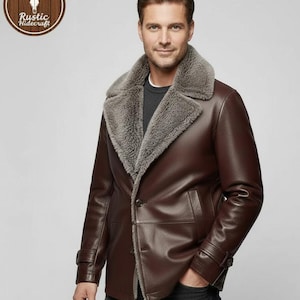 Peut inclure: Veste en cuir marron avec un col en peau de mouton grise. La veste a une fermeture à boutons, deux poches avant et un logo dans le coin supérieur gauche. La veste est portée par une personne.