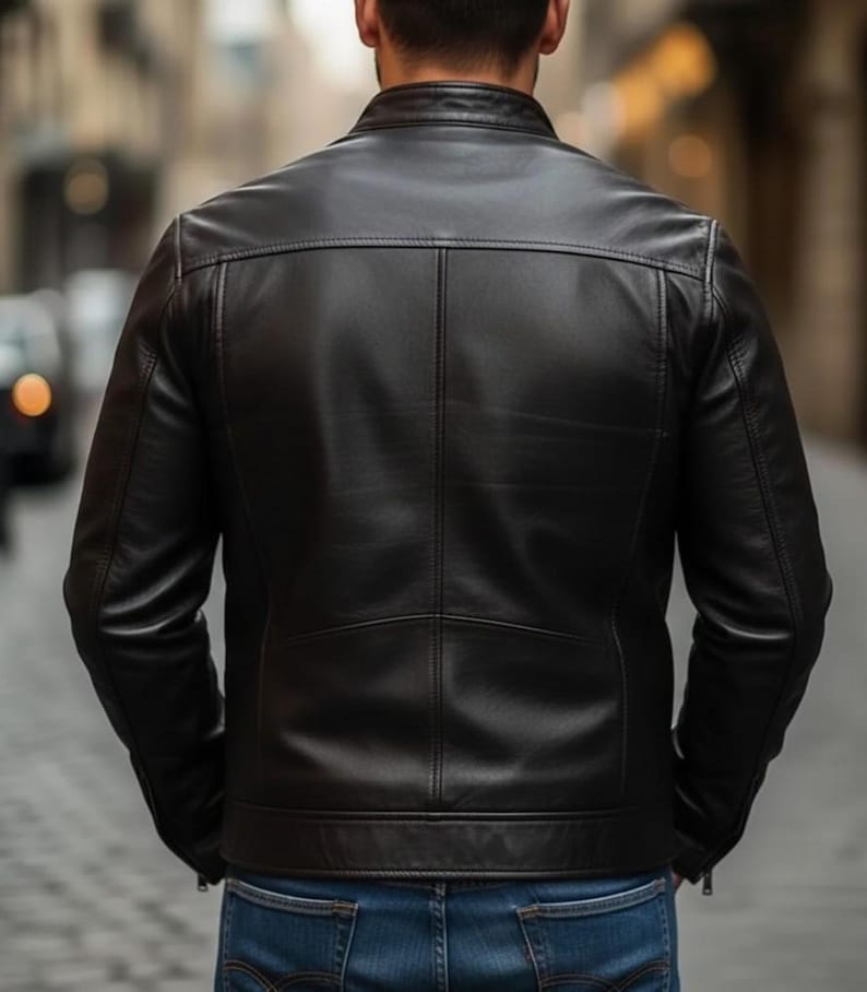 K&ouml;nnte beinhalten: Eine schwarze Lederjacke mit Stehkragen, langen &Auml;rmeln mit Rei&szlig;verschlussb&uuml;ndchen und einer horizontalen R&uuml;ckenpasse. Die Jacke verf&uuml;gt &uuml;ber eine mittige vertikale Naht auf dem R&uuml;ckenteil und wird mit einer blauen Jeans kombiniert.