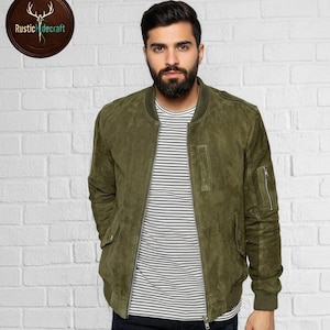May include: Olive green suede bomber jacket with a zip closure, side pockets, and a ribbed collar and cuffs. The jacket is worn over a striped shirt. The Rustic Hidecraft logo is in the upper left corner.