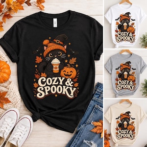 Peut inclure: Un t-shirt noir à manches courtes avec un motif représentant un chat noir portant un bonnet orange et un chapeau de sorcière, tenant un gobelet de café près d'une citrouille, de feuilles d'automne et de chauves-souris, avec le texte "COZY & SPOOKY".