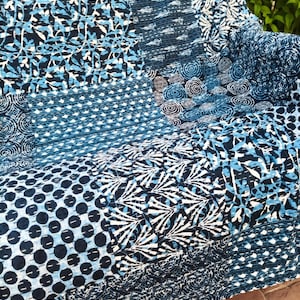 May include: A patchwork quilt featuring various shades of indigo blue and white fabric panels. The textile displays a variety of geometric patterns, including circular swirls, dotted lines, leaf-like shapes, and abstract botanical motifs.